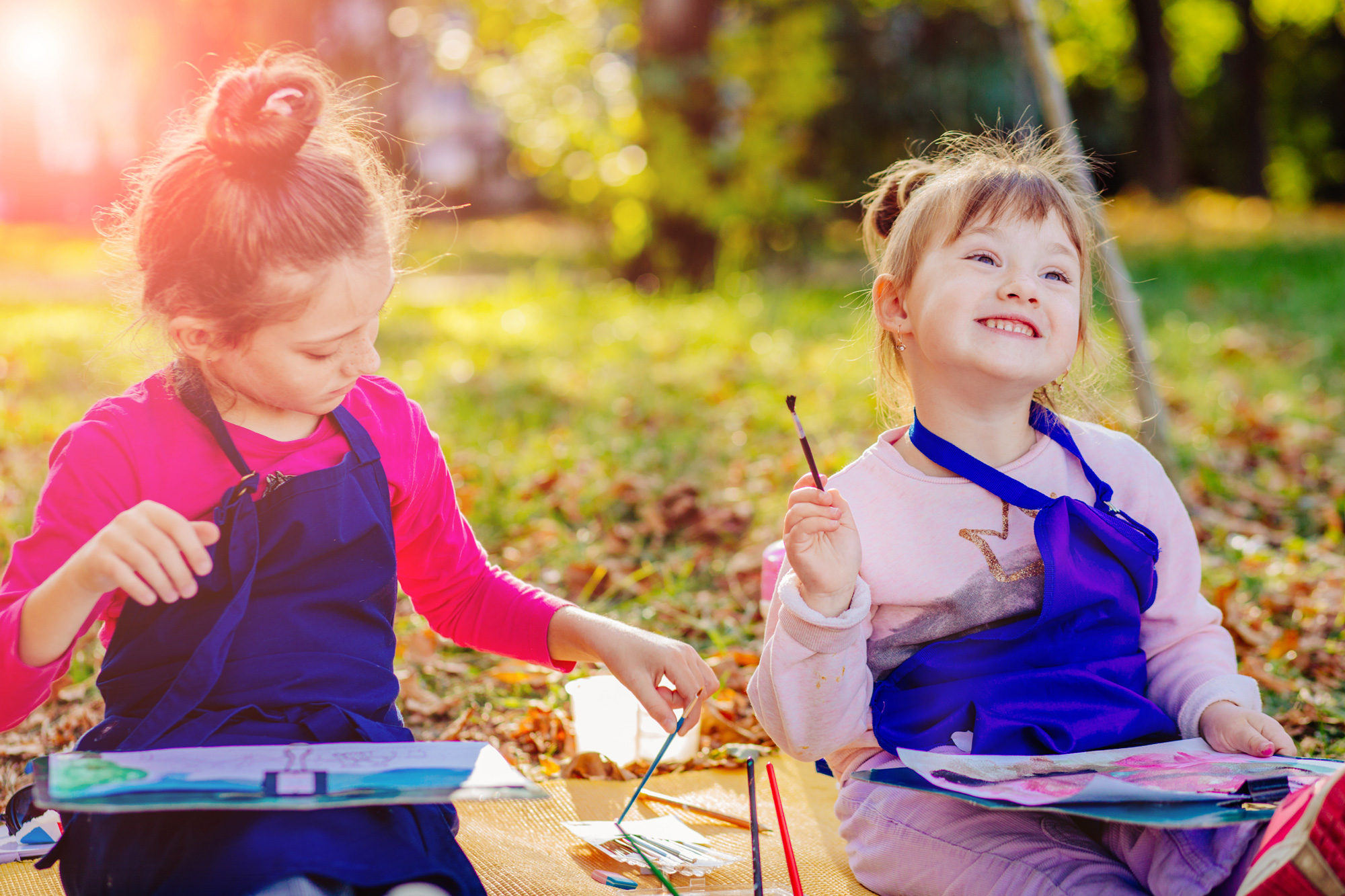 Two preschool girls drawing together in the fall outside on a blanket in a park.